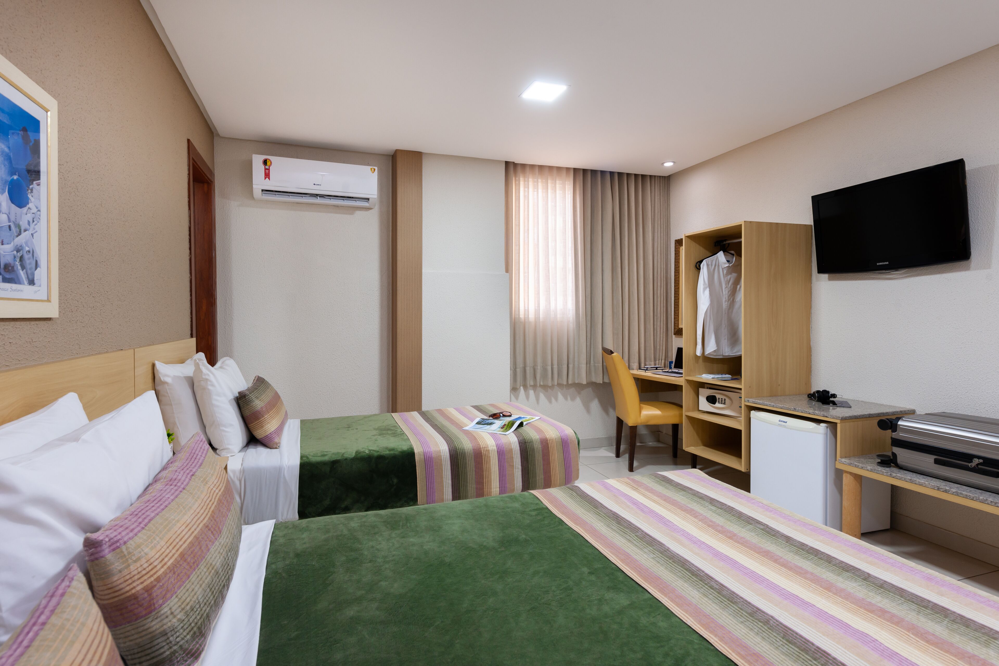 Une chambre d’hôtel avec deux lits, un bureau, une chaise, une télévision et un petit réfrigérateur.