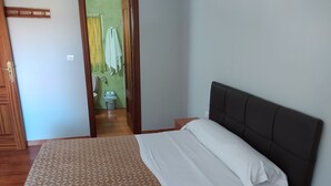 A hotel room with a bed, a wooden door, and a bathroom visible through an open door.