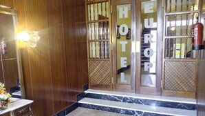 A wooden door with "HOTEL EUROPA" signage, a marble floor, and a small table with a vase of flowers.