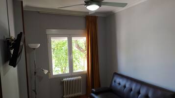 Un salon avec un canapé marron foncé, un lampadaire, un ventilateur de plafond, un radiateur et une fenêtre avec des rideaux.