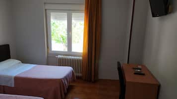 Une chambre d’hôtel avec deux lits, un bureau, une chaise, un téléviseur fixé au mur et une fenêtre avec des rideaux.