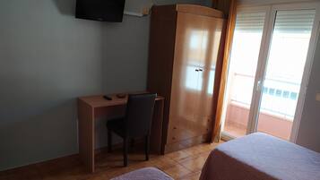 Een kamer met een houten bureau, een stoel, een kledingkast, een televisie aan de muur en twee bedden met beddengoed met een patroon.