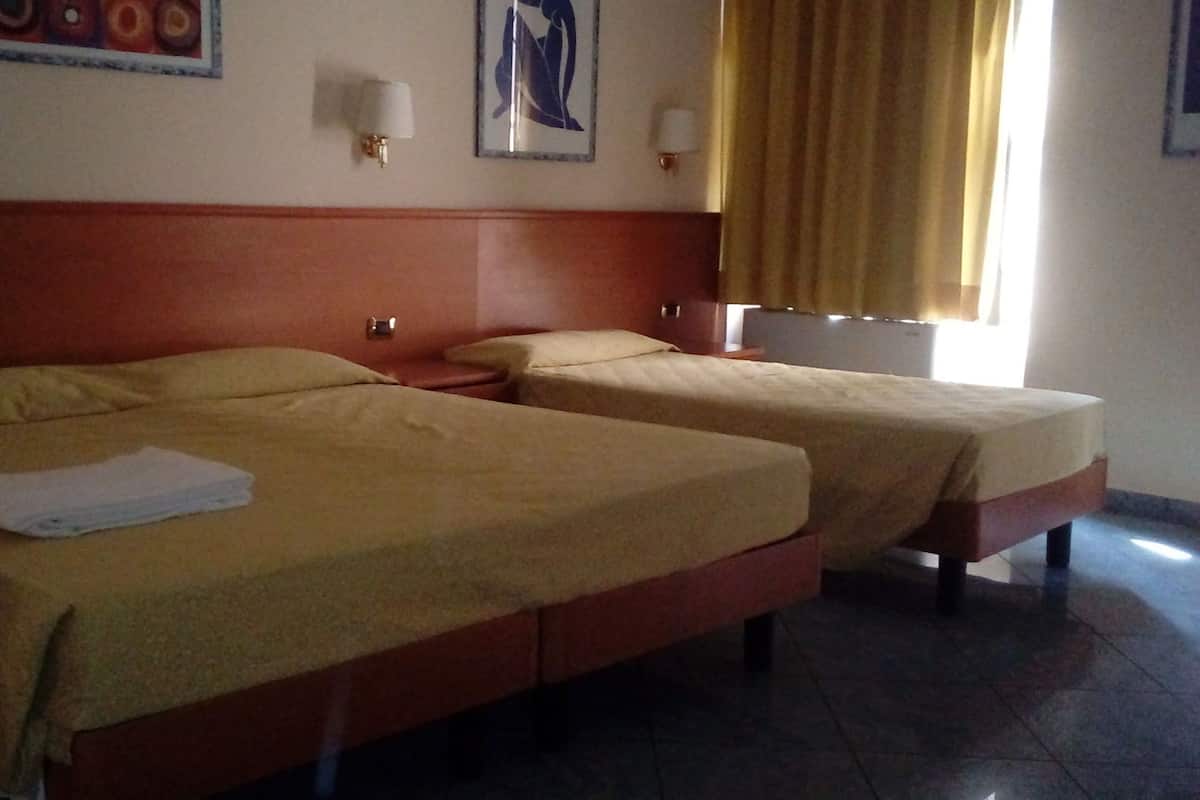 A hotel room with two single beds, a wooden headboard, a wall-mounted lamp, and a window with curtains.