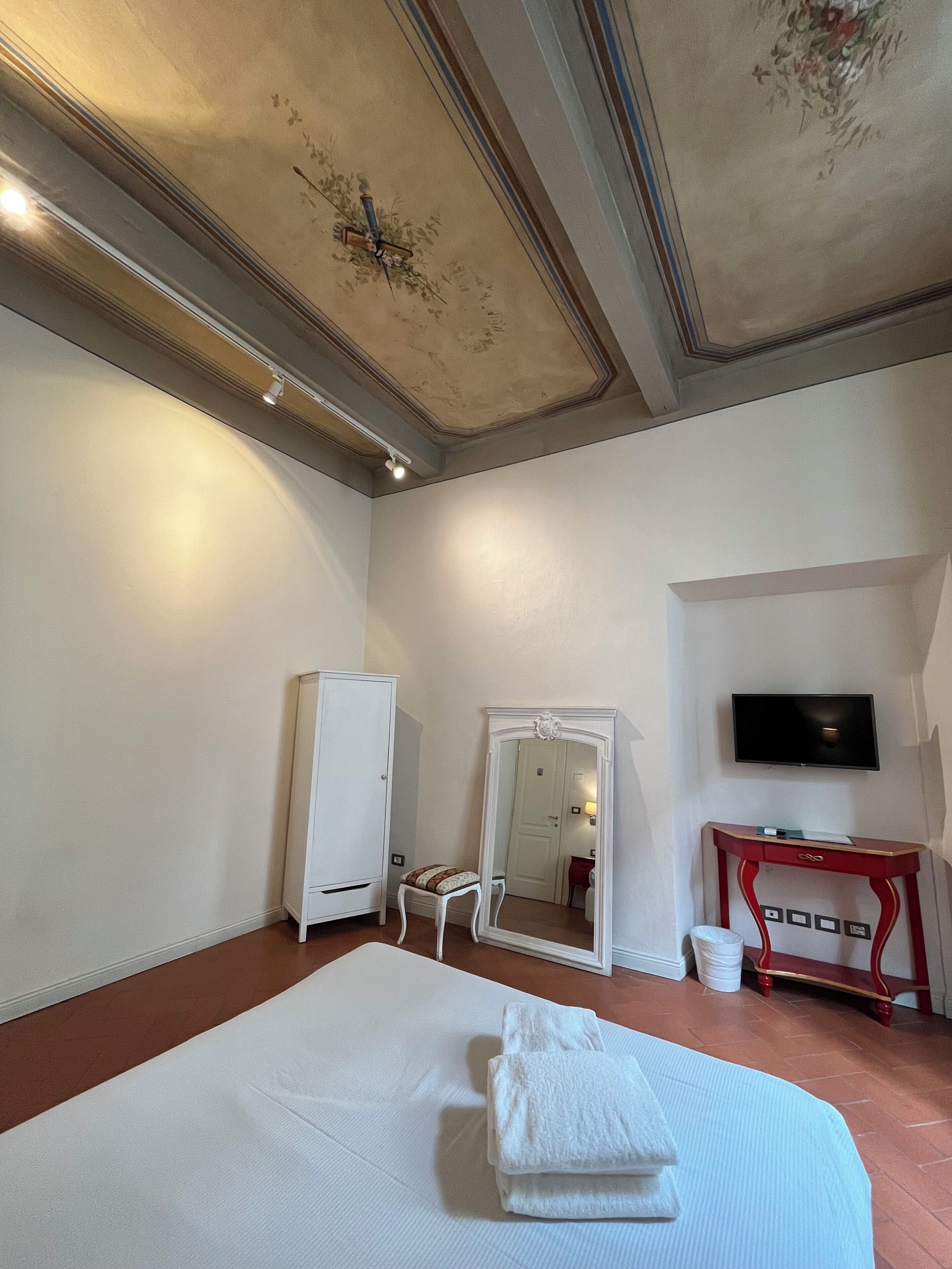 A bedroom with a bed, a wardrobe, a mirror, a television, and a desk.