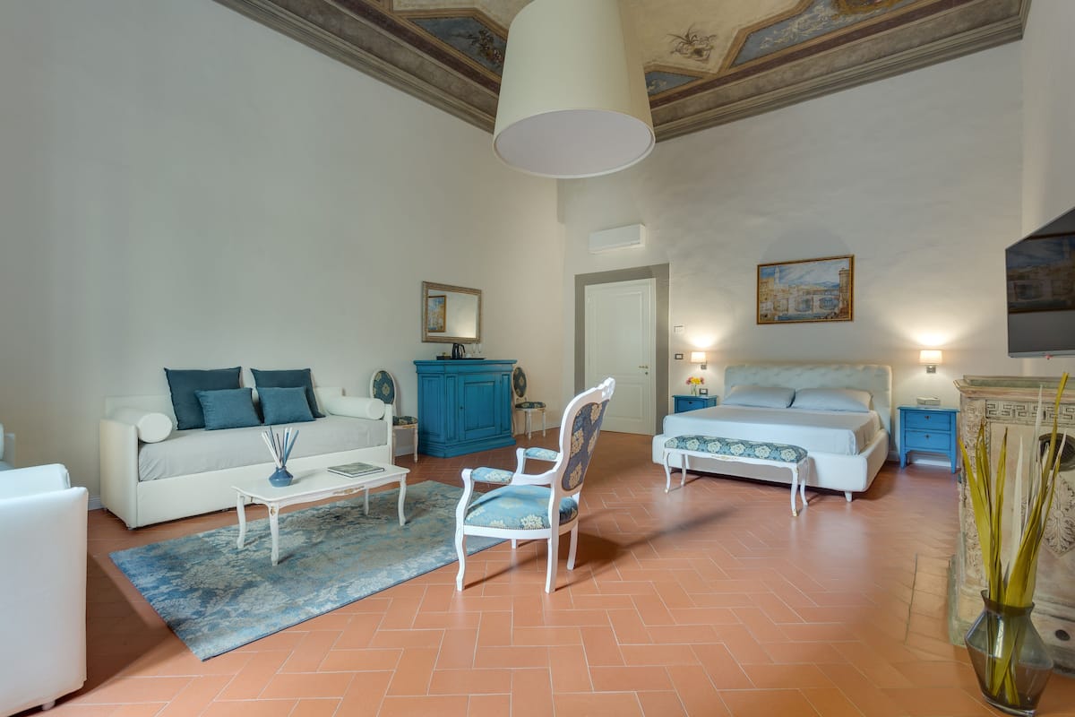A spacious living room with a sofa, a chair, a coffee table, a bed, and a blue cabinet.