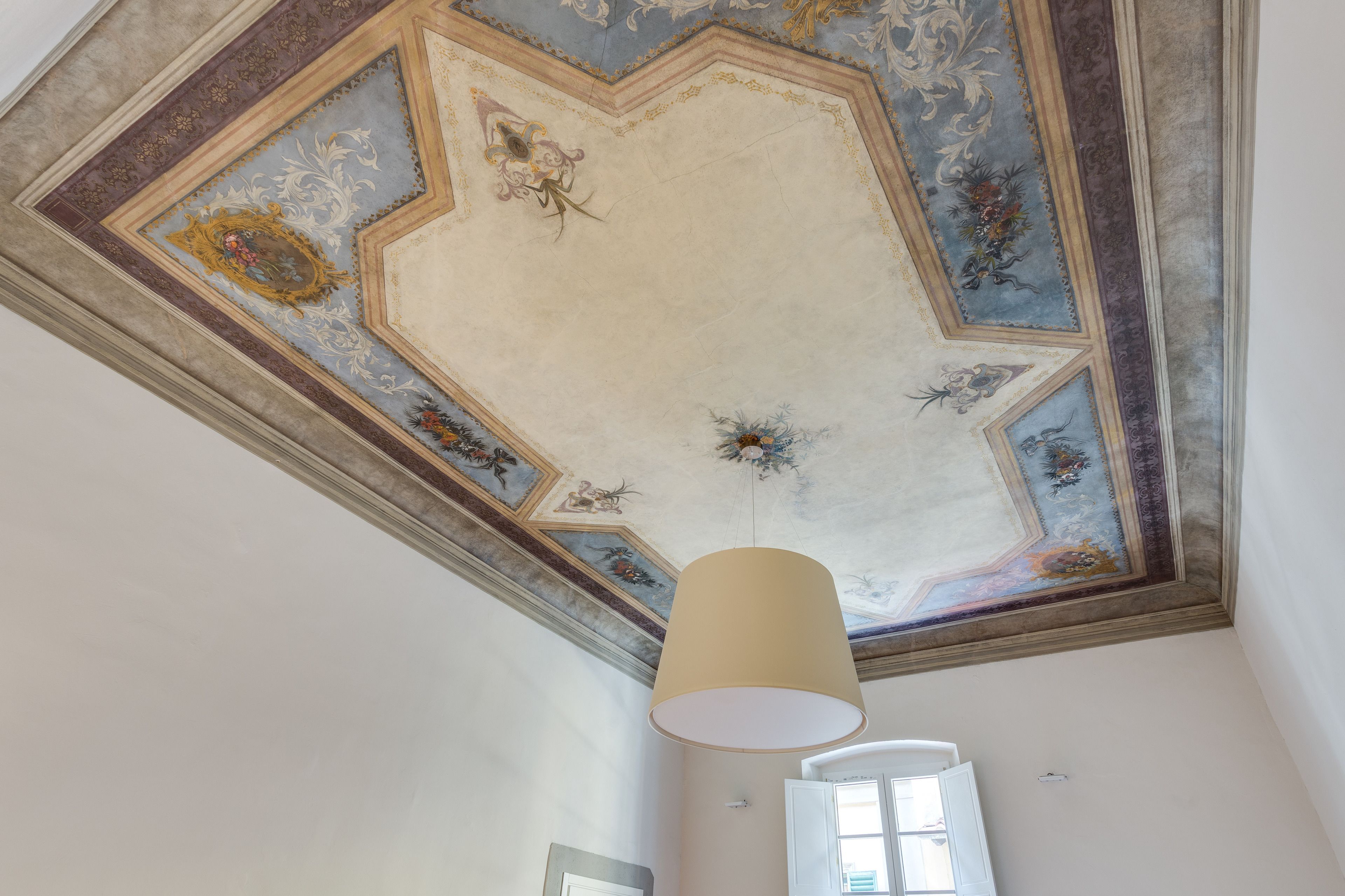 A room with a decorative ceiling featuring floral and geometric patterns.