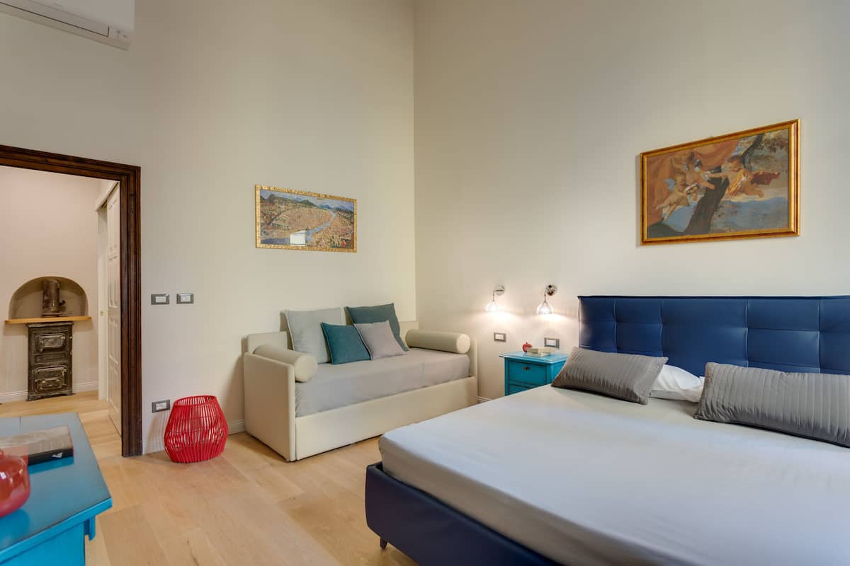 A bedroom with a bed, a sofa, a nightstand, and a painting on the wall.