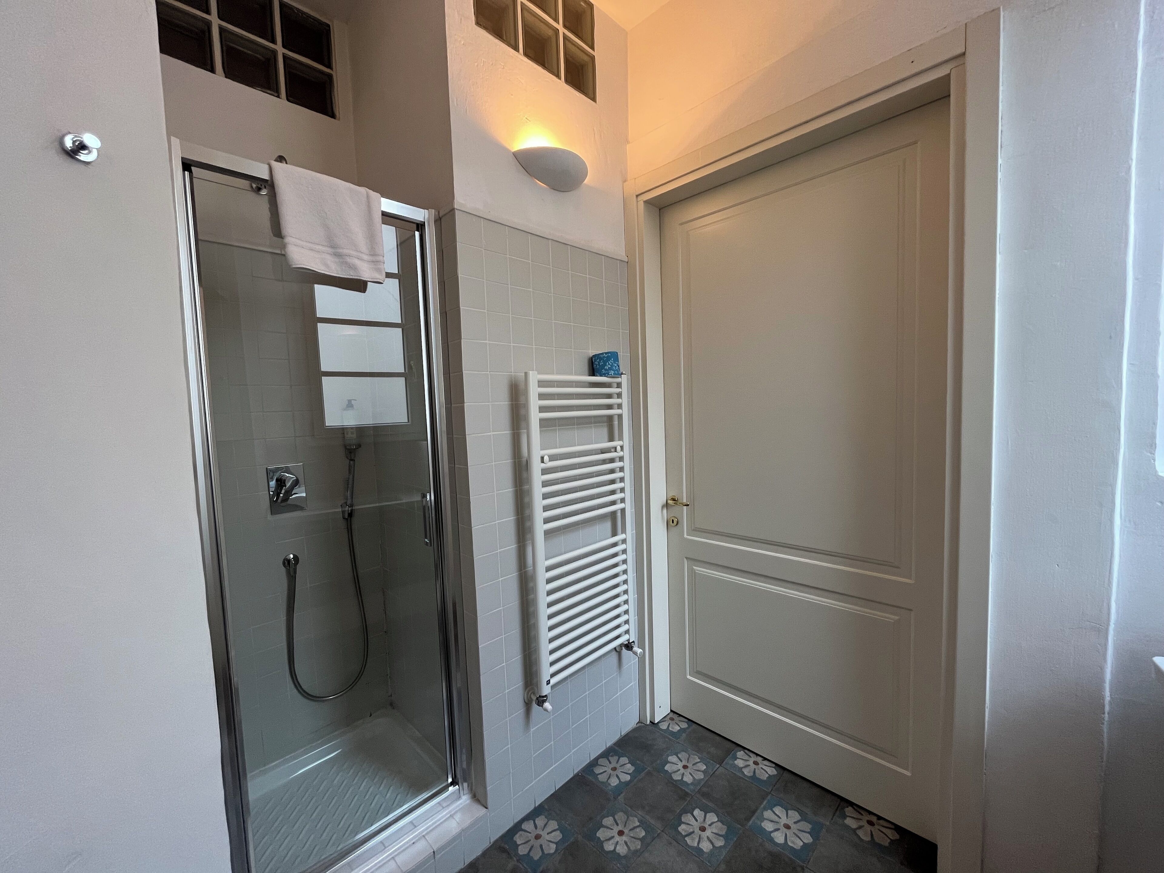 A bathroom with a glass-enclosed shower, a white door, and a tiled floor with a floral pattern.