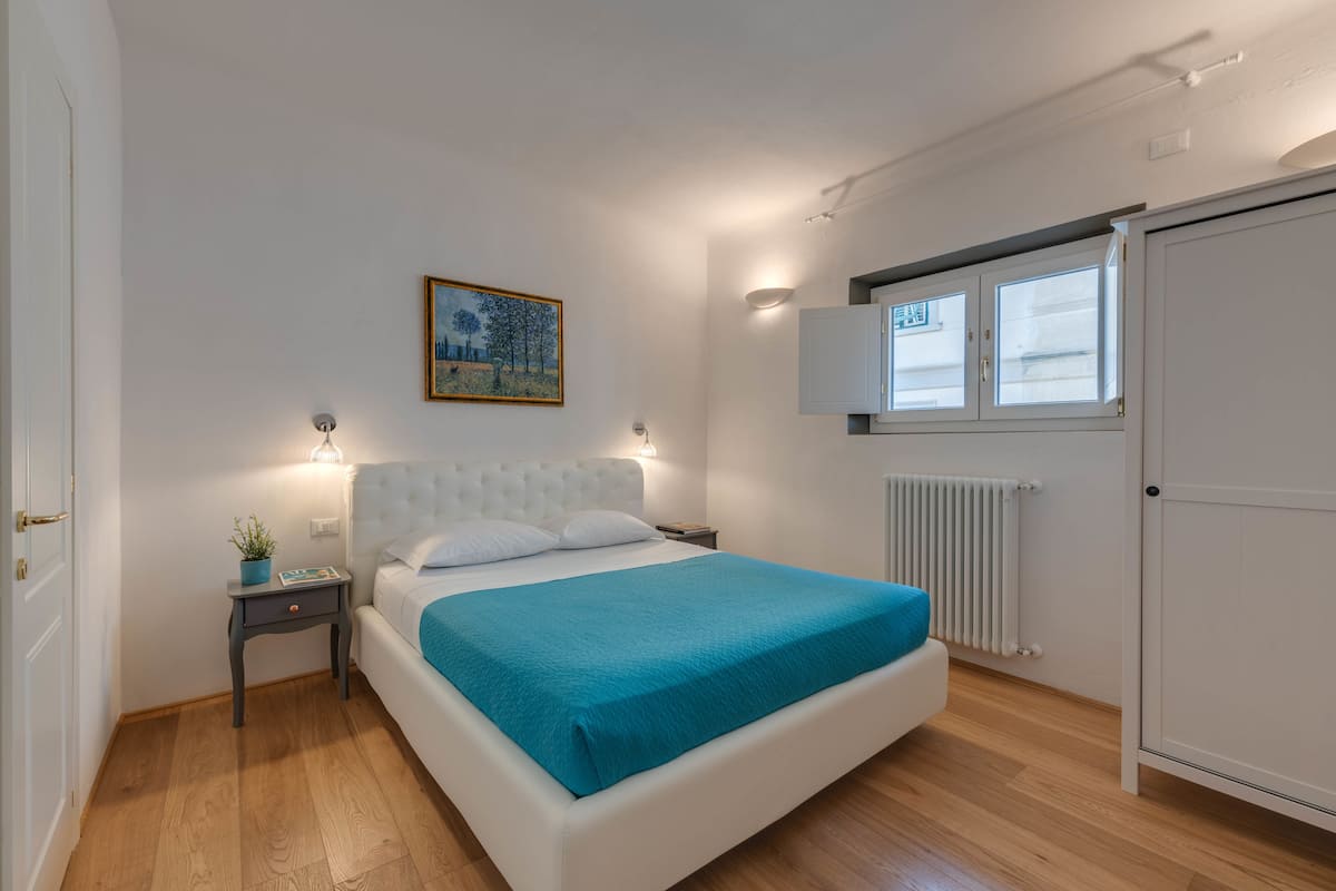 A bedroom with a bed, bedside tables, a radiator, and a wardrobe.