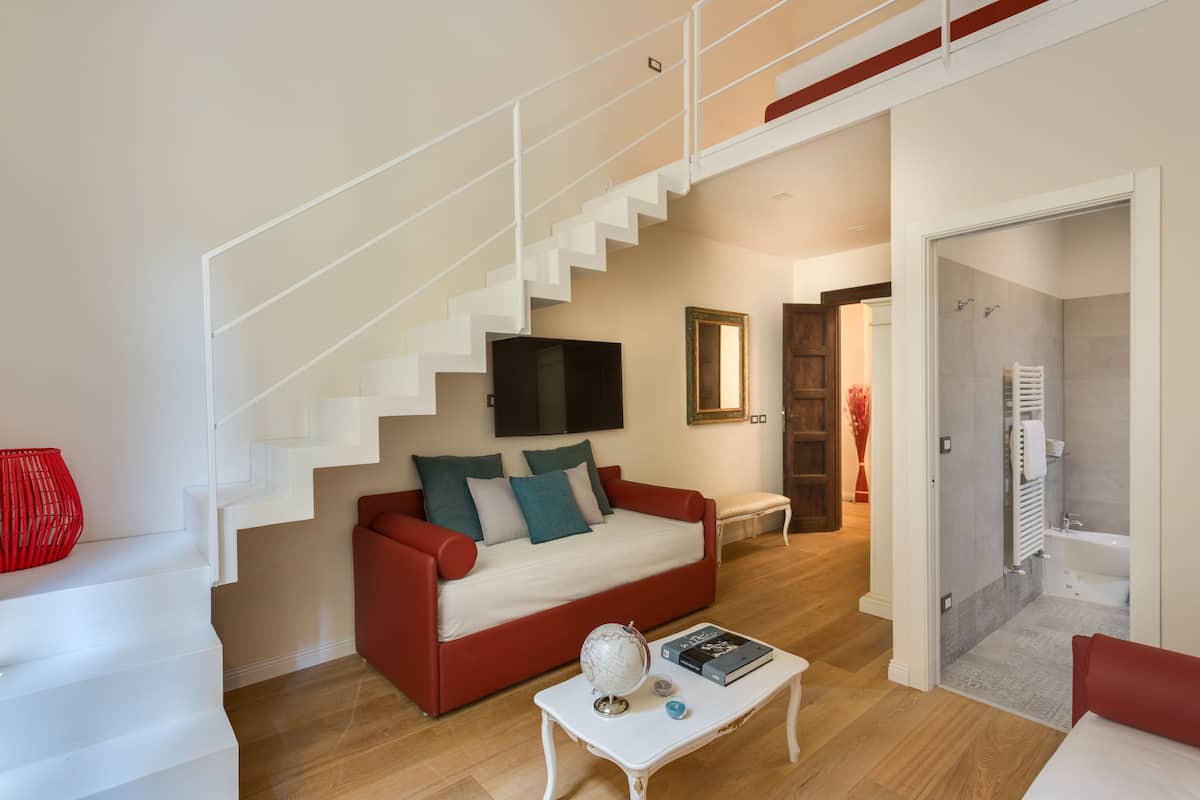 A modern living room with a staircase, a red sofa, a white coffee table, and a TV mounted on the wall.