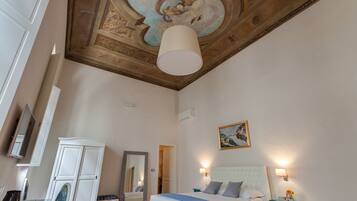 Una habitación de hotel con una cama grande, un armario, un espejo, un techo con un fresco y luces instaladas en la pared.