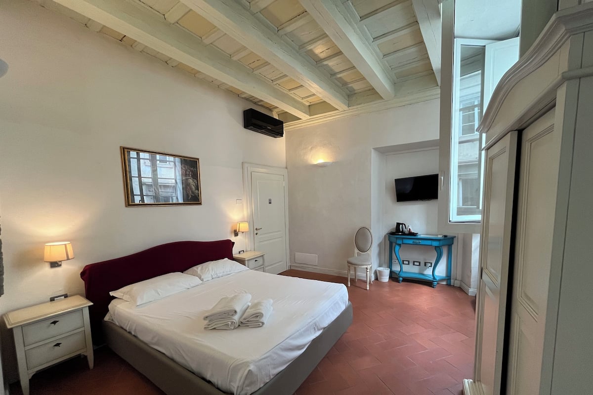 A hotel room with a large bed, a desk with a chair, a television, and a window.