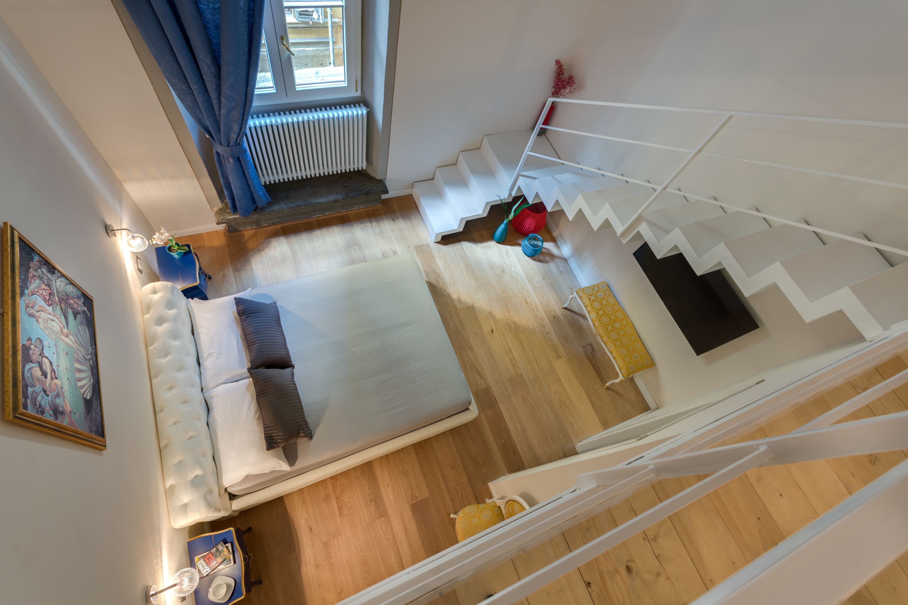 A bedroom with a bed, a nightstand, a window with curtains, a radiator, and a staircase.