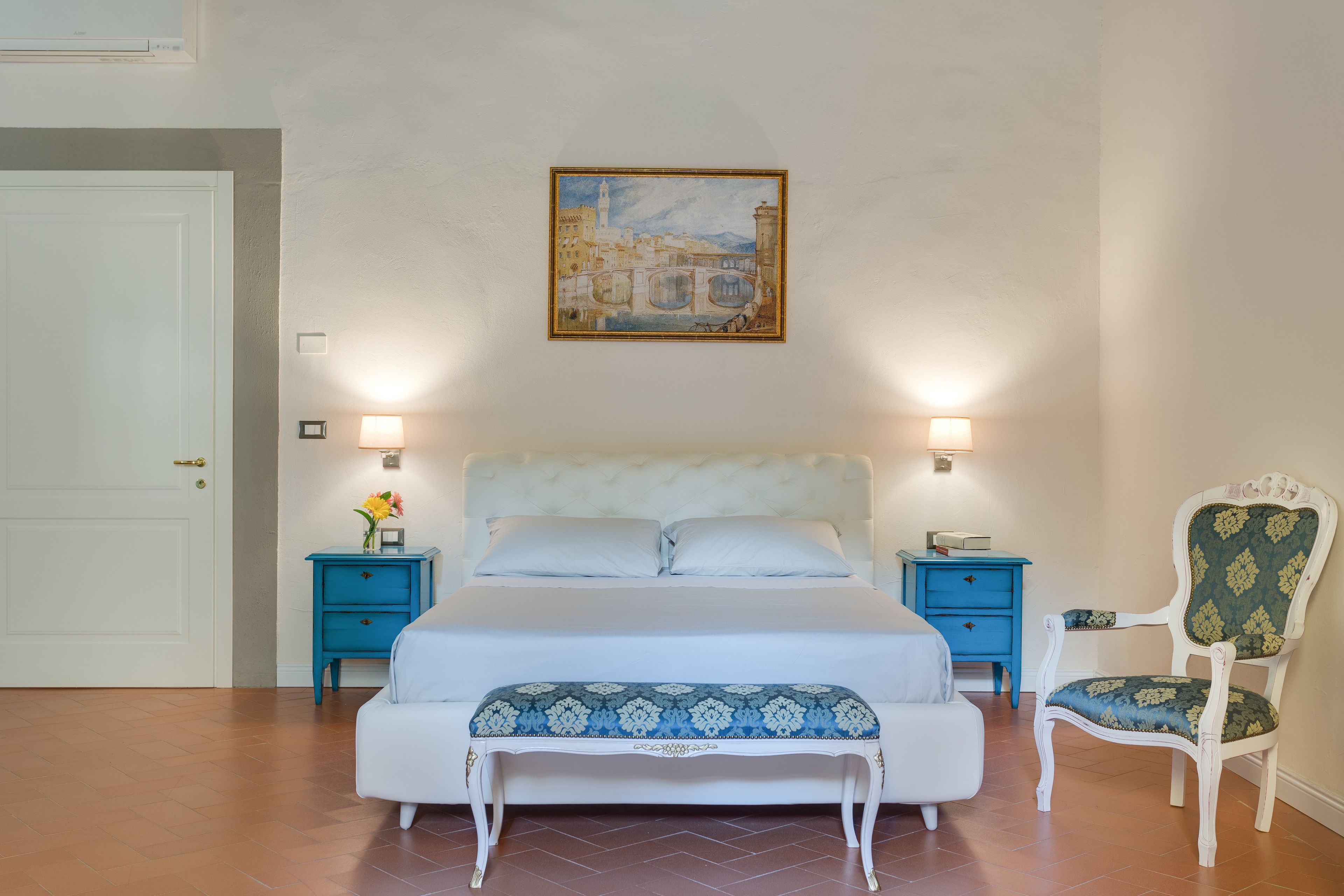 Una camera da letto con un letto, comodini, una sedia, una panca e un quadro appeso al muro.