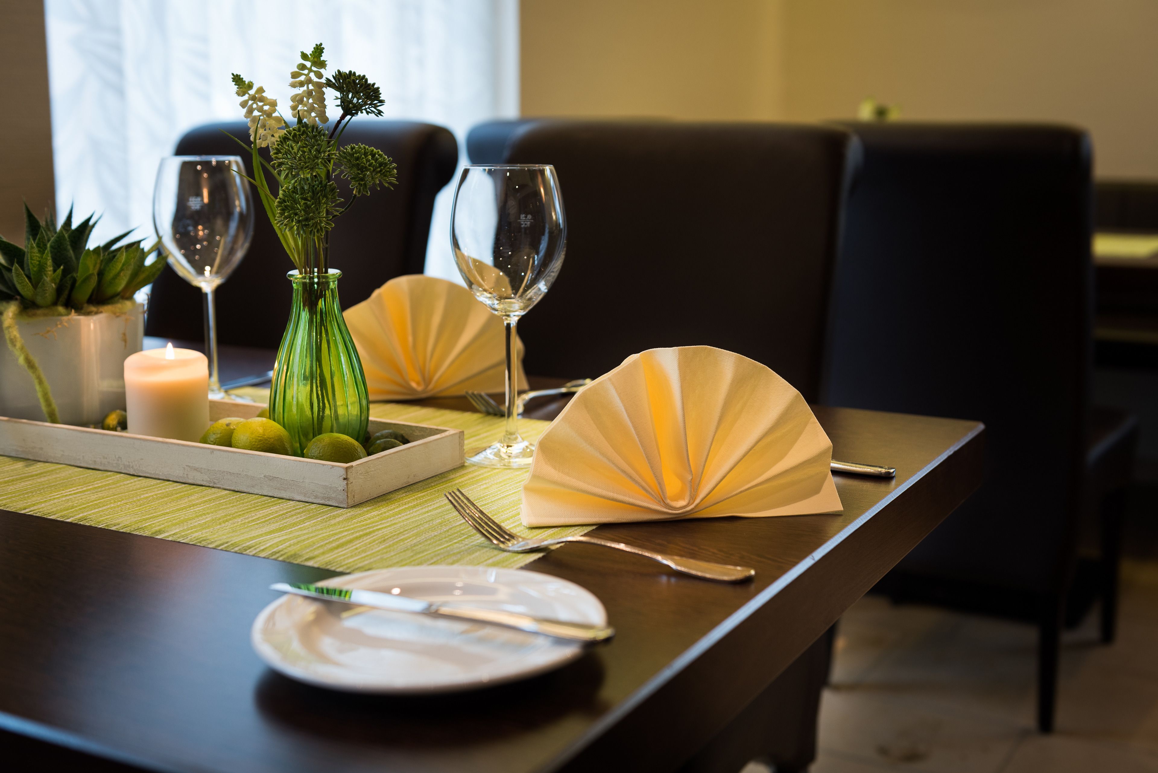 A dining table set with a candle, a vase with flowers, and two wine glasses.