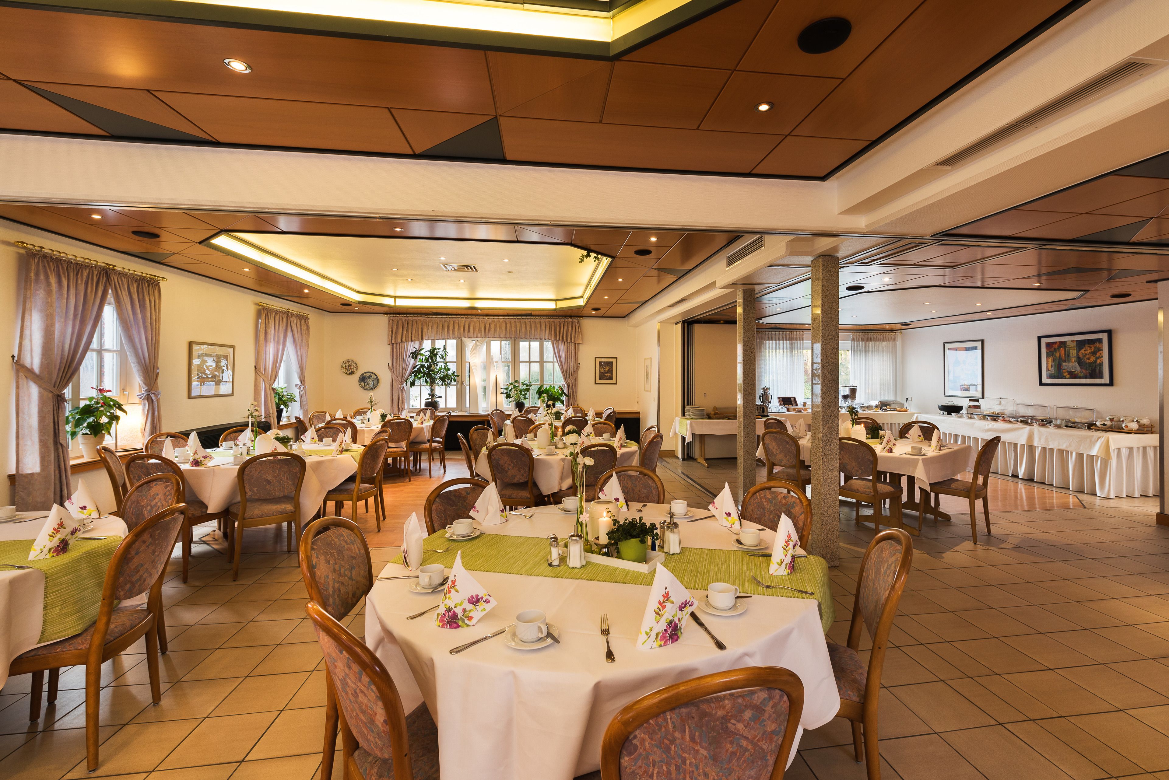 Une grande salle à manger avec de nombreuses tables dressées pour un repas, et dont l’aménagement est propre et bien organisé.