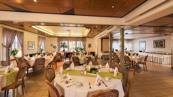 Une grande salle à manger avec de nombreuses tables dressées pour un repas, et dont l’aménagement est propre et bien organisé.