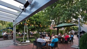 An outdoor patio area with brick flooring, metal tables, and chairs. - Hotel Nagel (Sudlohn)