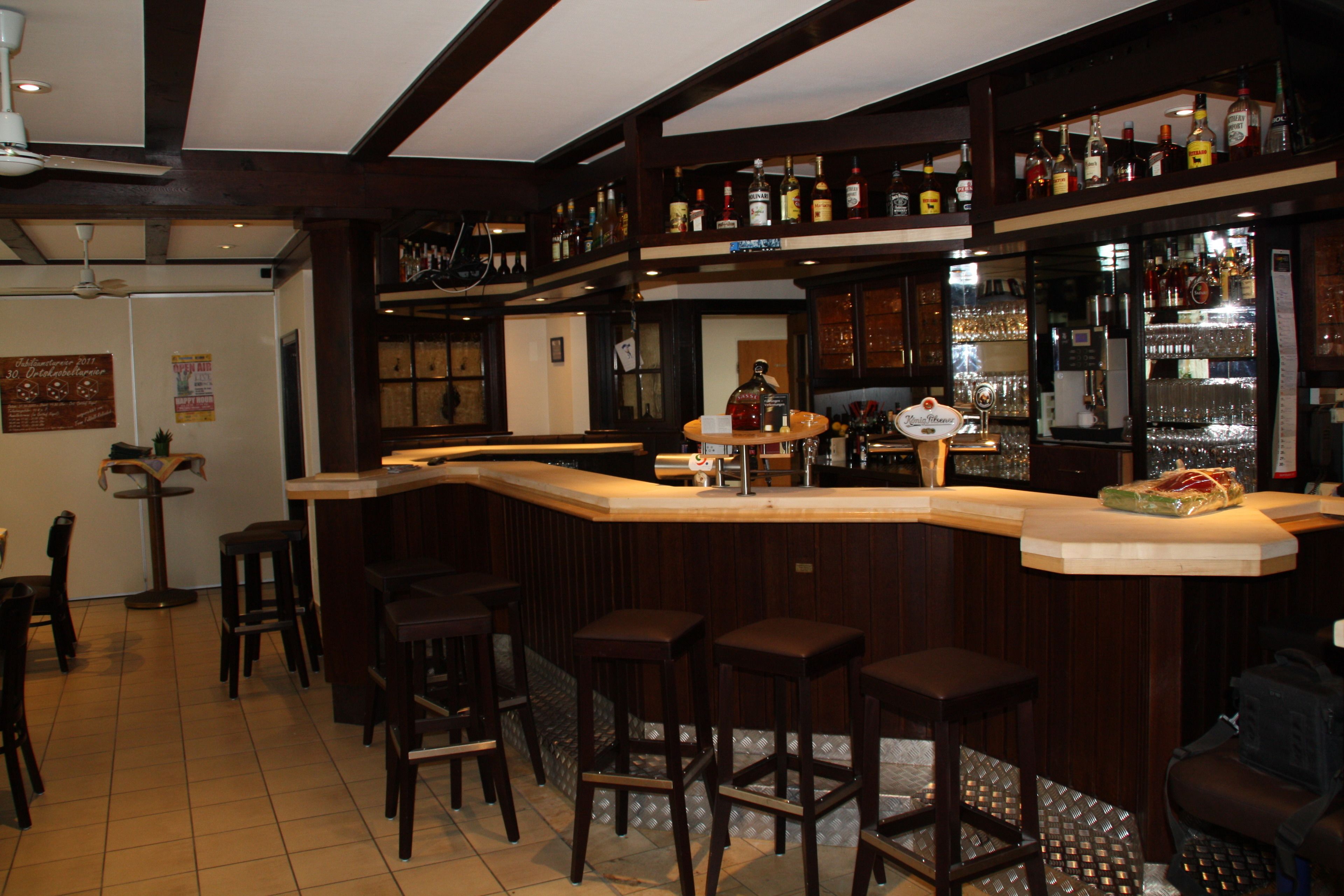 Una zona de bar con taburetes de madera, una barra y estantes llenos de botellas.