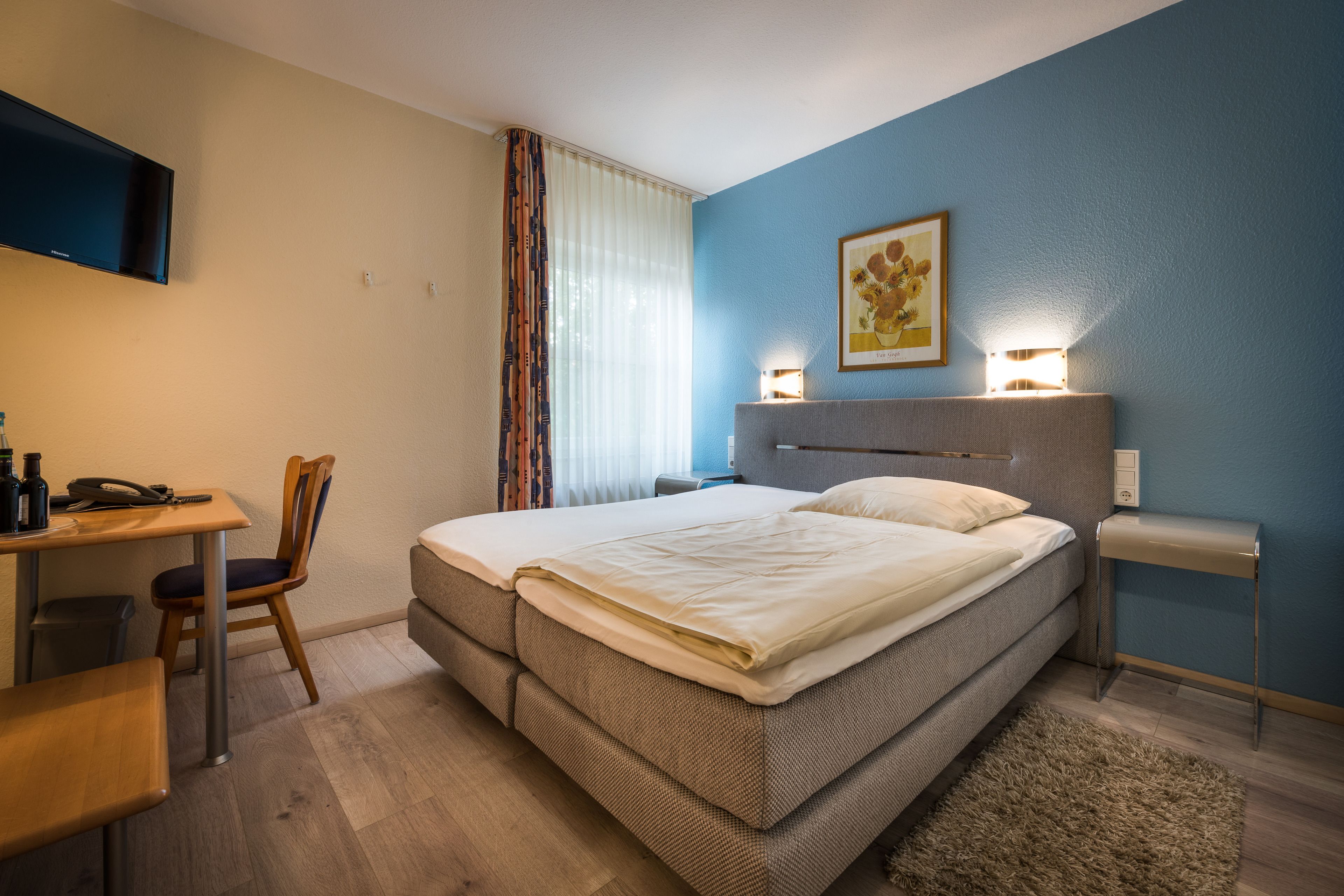 A neatly arranged hotel room with a bed, a desk, a chair, and a television.