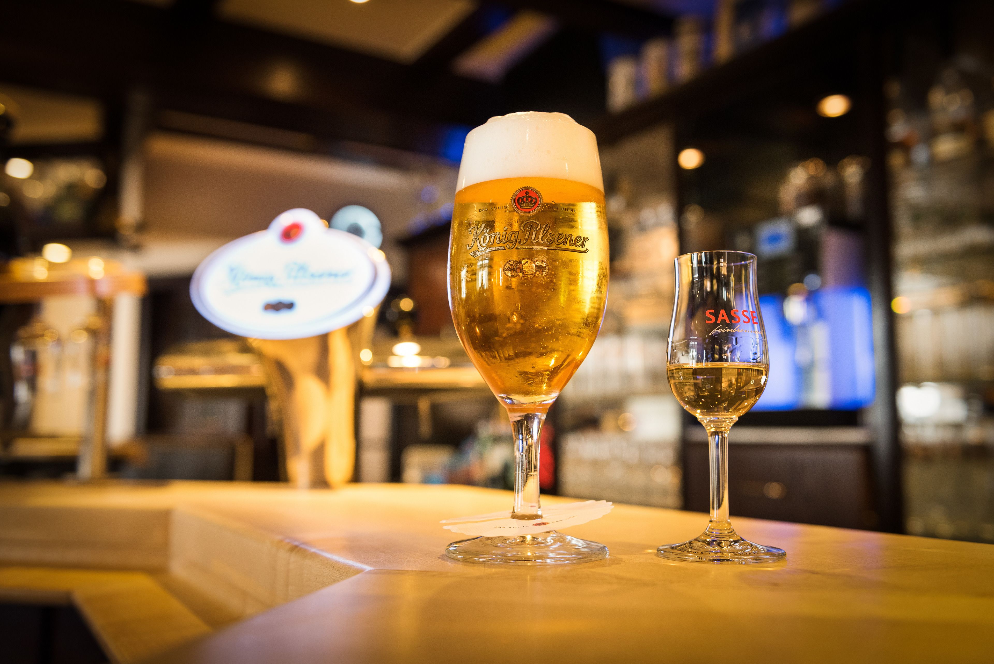 Zwei Biergläser auf einer Bar, unscharfer Hintergrund.