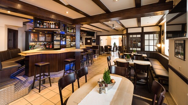A bar area with a counter, stools, and a variety of bottles. There are tables and chairs arranged for dining. - Hotel Nagel (Sudlohn)