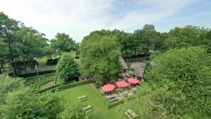 Een weelderige tuin met een tuinhuisje, strak bijgesnoeide hagen en een vlaggenmast.