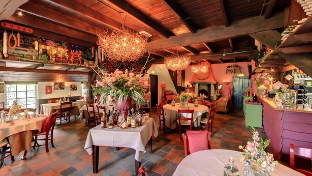 Een gezellig restaurant met houten balken, ronde tafels en bloemrijke decoraties.
