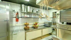 Een moderne keuken met roestvrijstalen apparatuur, hangende pannen en manden met fruit op het aanrecht.