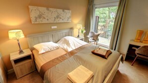Een hotelkamer met een groot bed, twee nachtkastjes, een stoel, een raam met gordijnen en uitzicht op groen.