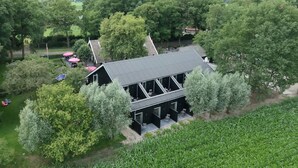 Een gebouw met twee verdiepingen, voorzien van een donker dak en vele ramen, omgeven door weelderige begroeiing en bomen.