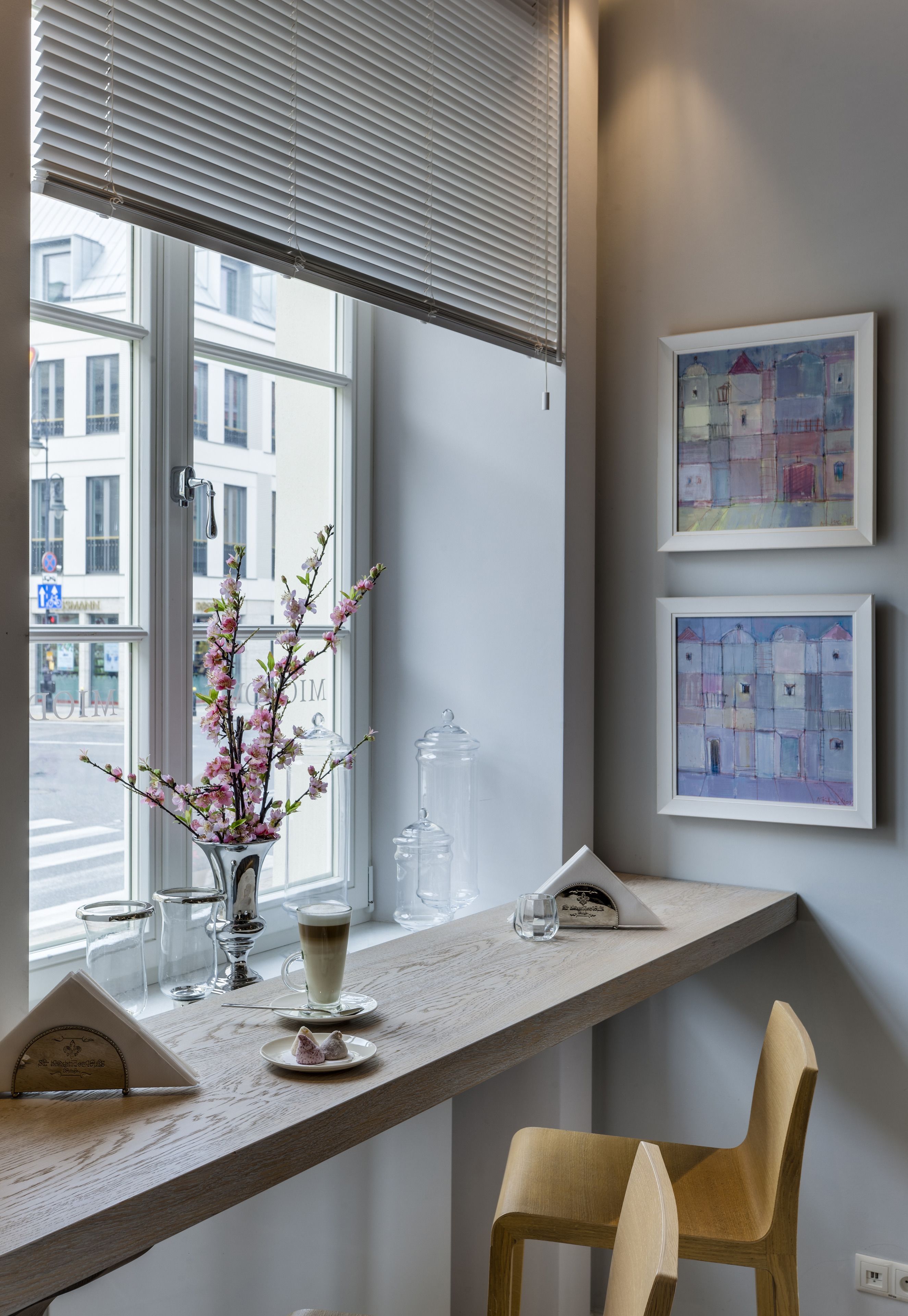 A modern room with a wooden desk, a vase with flowers, a cup of coffee, and two framed artworks on the wall.
