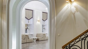 Suuri aula, jossa on ruutukuviollinen lattia, mustalla kaiteella varustettu portaikko ja seinään kiinnitetty valaisin.
