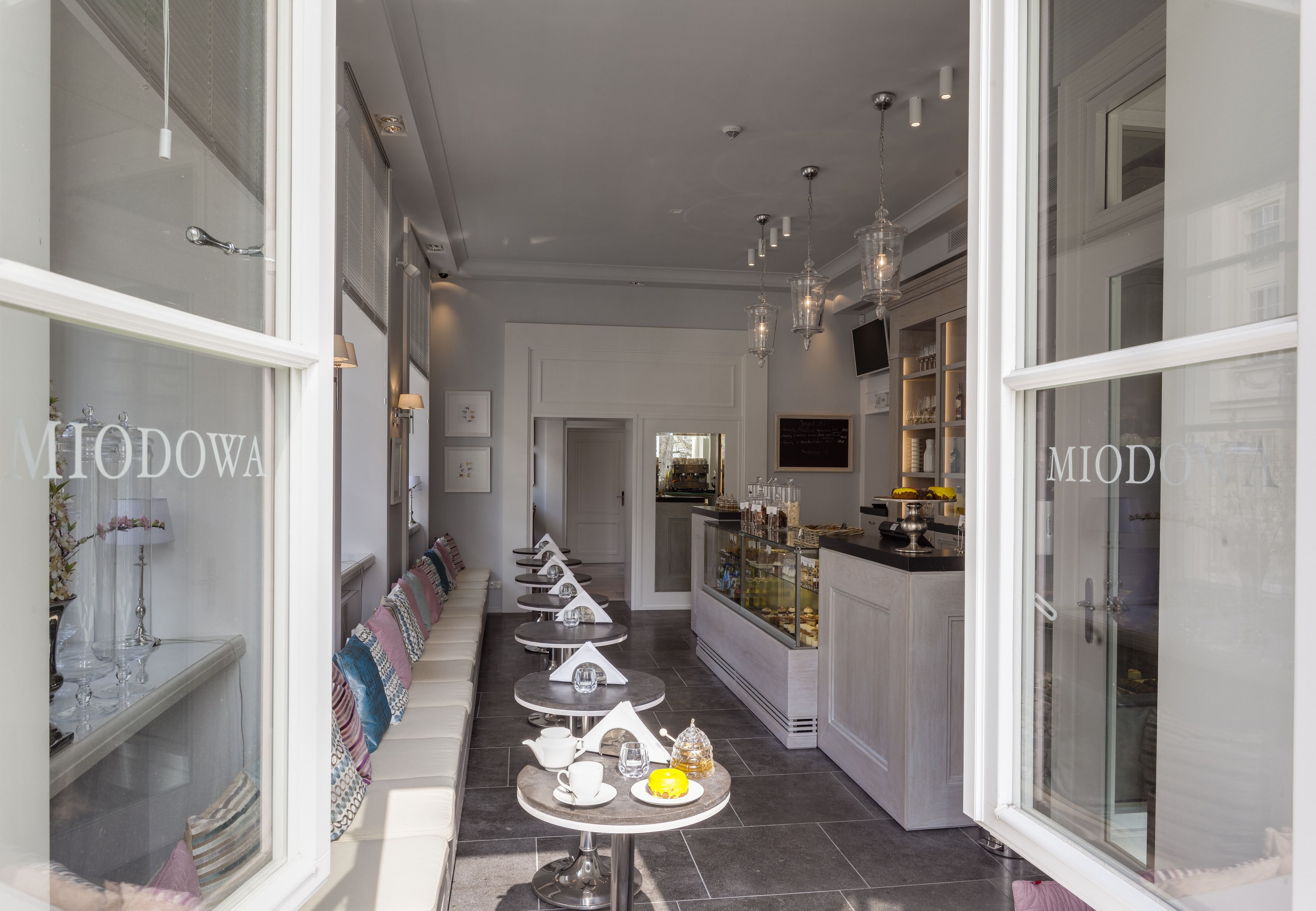 A corridor with a series of small tables and chairs, a glass display case with pastries, and a counter with various items.