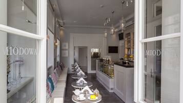 A corridor with a series of small tables and chairs, a glass display case with pastries, and a counter with various items.