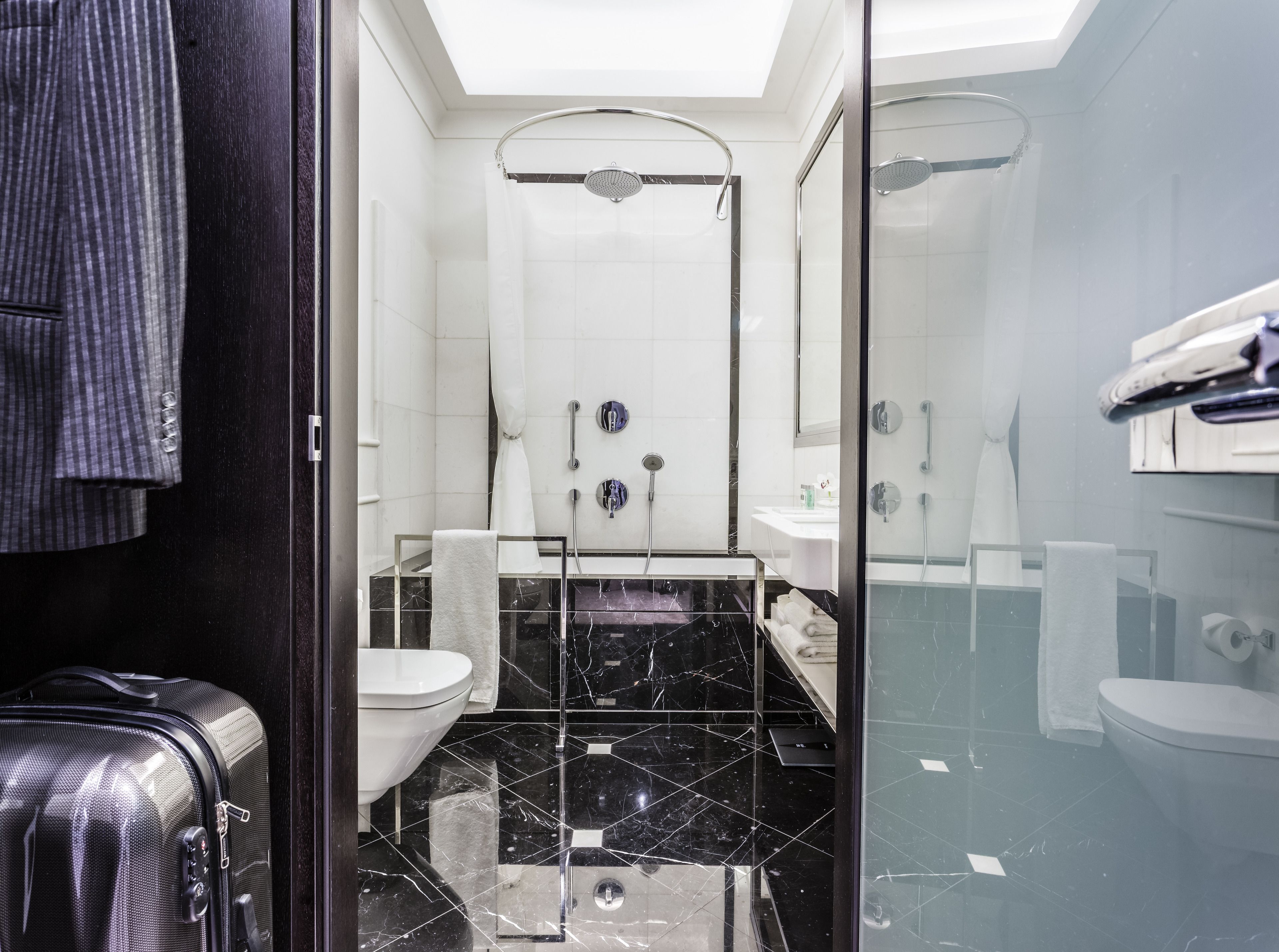 Un baño moderno con cabina de ducha de vidrio, inodoro blanco y lavamanos de mármol negro.