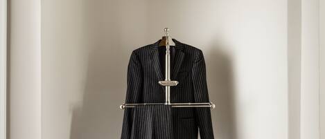 A room with a coat stand holding a pinstriped suit, two wall-mounted lamps, and a pair of shoes on the floor.