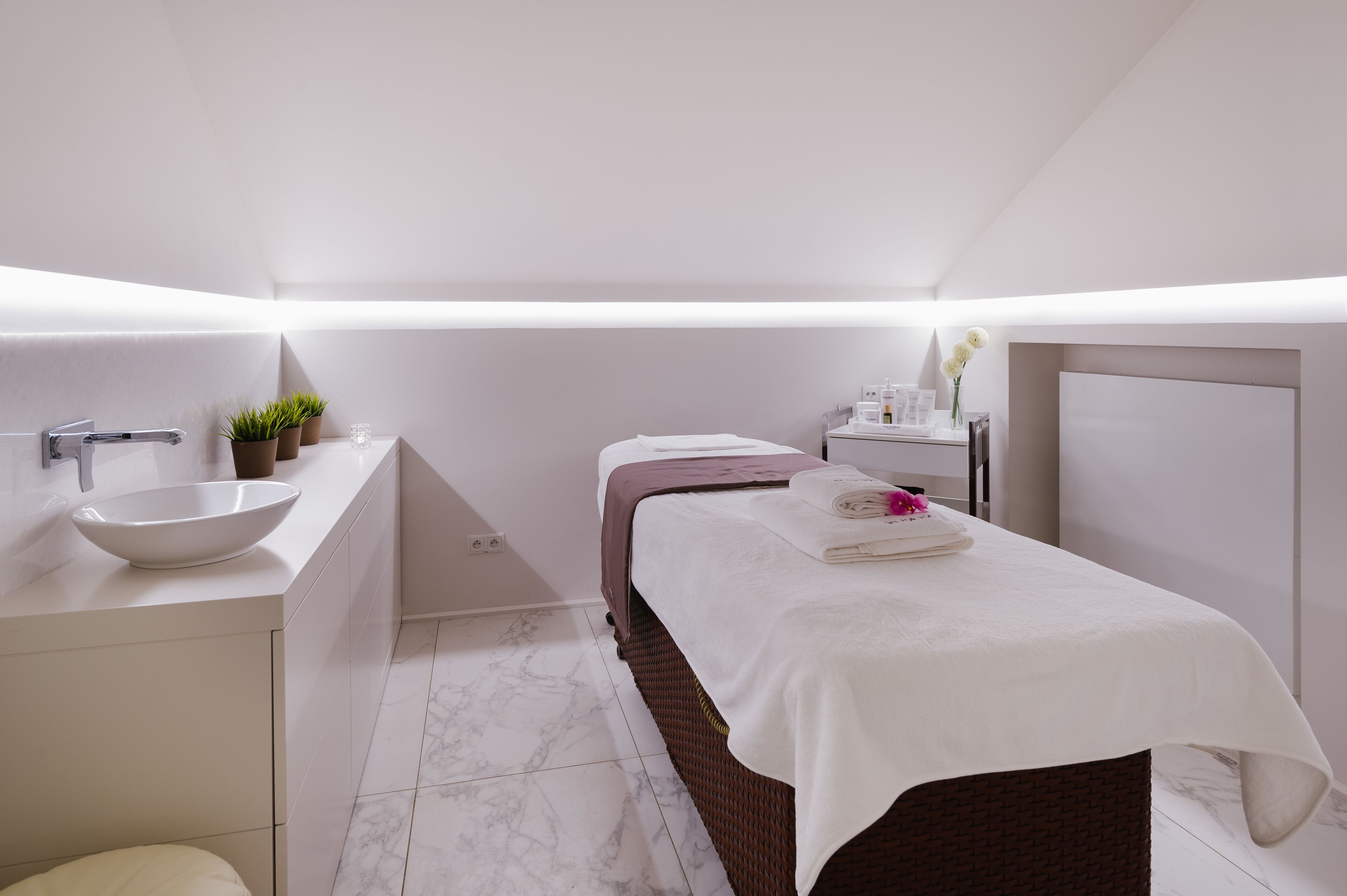 A modern, minimalist bedroom with a large bed, a bedside table, a built-in sink, and a small potted plant.