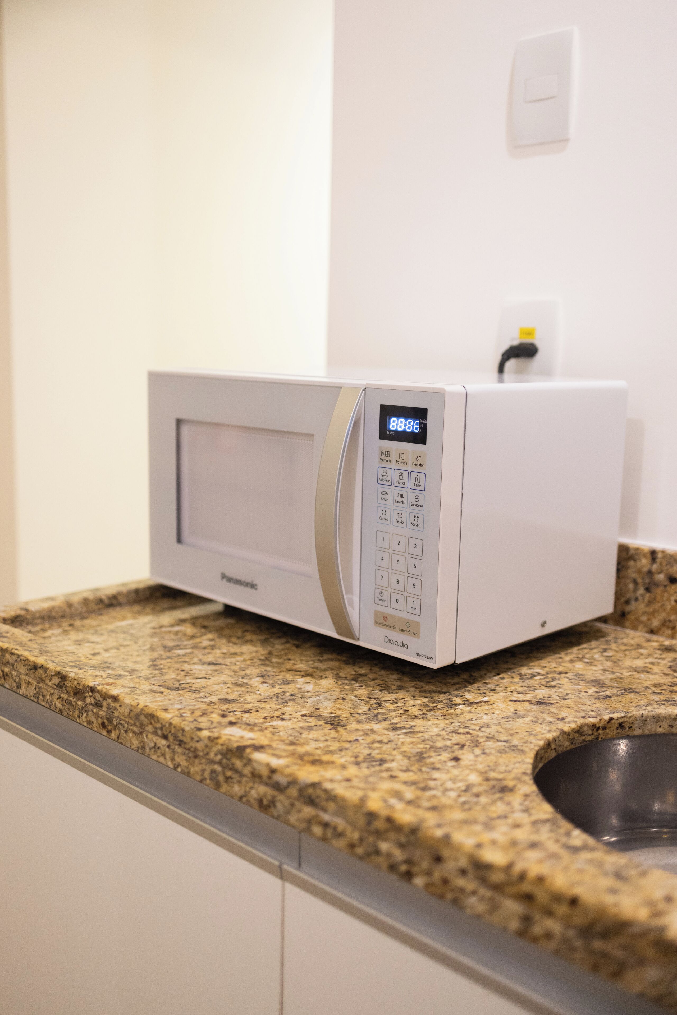 A white microwave on a granite countertop in a kitchen.