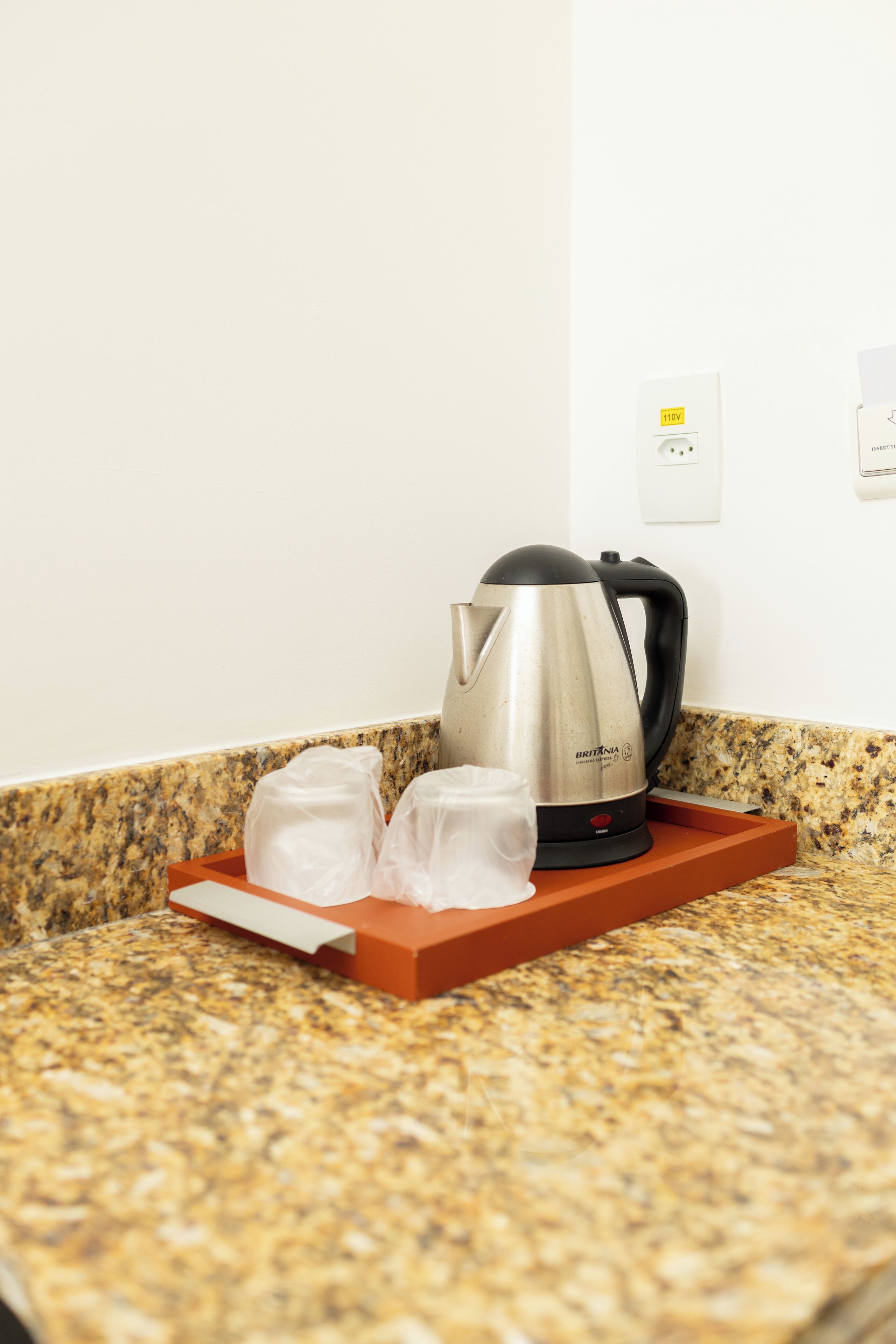 A kitchen counter with a stainless steel kettle, two plastic bags, and a red tray.