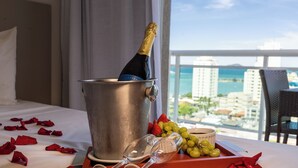 A bed with a champagne bottle in a bucket, a glass, and a tray with grapes and strawberries. -  Transamerica Executive Macaé (Macaé)