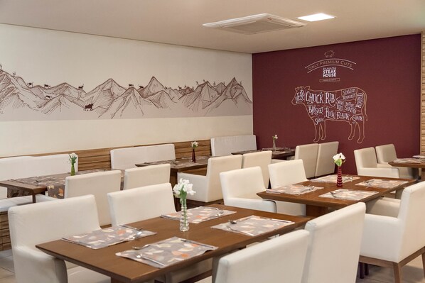A restaurant with white chairs and tables, a wall mural of mountains and animals, and a sign for "RAMADA STEAK HOUSE."