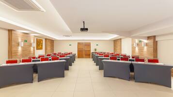 Un salón de conferencias con mesas y sillas dispuestas en filas, un proyector y paneles de madera en las paredes.