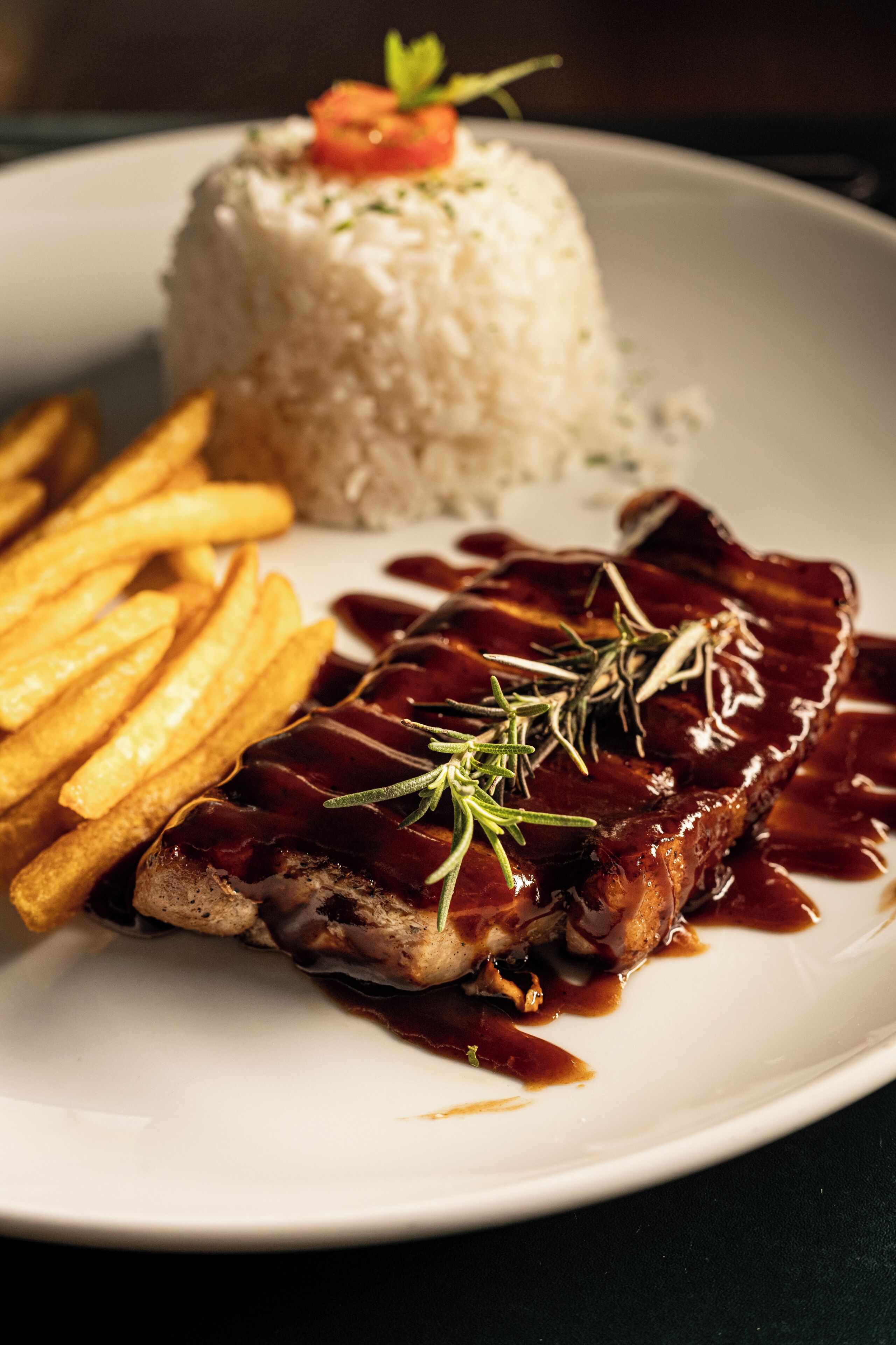 A plate with a piece of meat topped with sauce and herbs, a mound of rice, and a side of French fries.