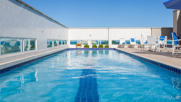 A swimming pool with clear blue water, surrounded by white walls and a tiled deck. -  Transamerica Executive Macaé (Macaé)