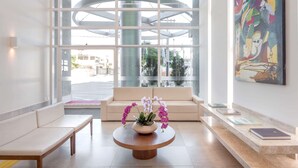 A modern lobby with a round wooden table, a beige sofa, and a large abstract painting. -  Transamerica Executive Macaé (Macaé)