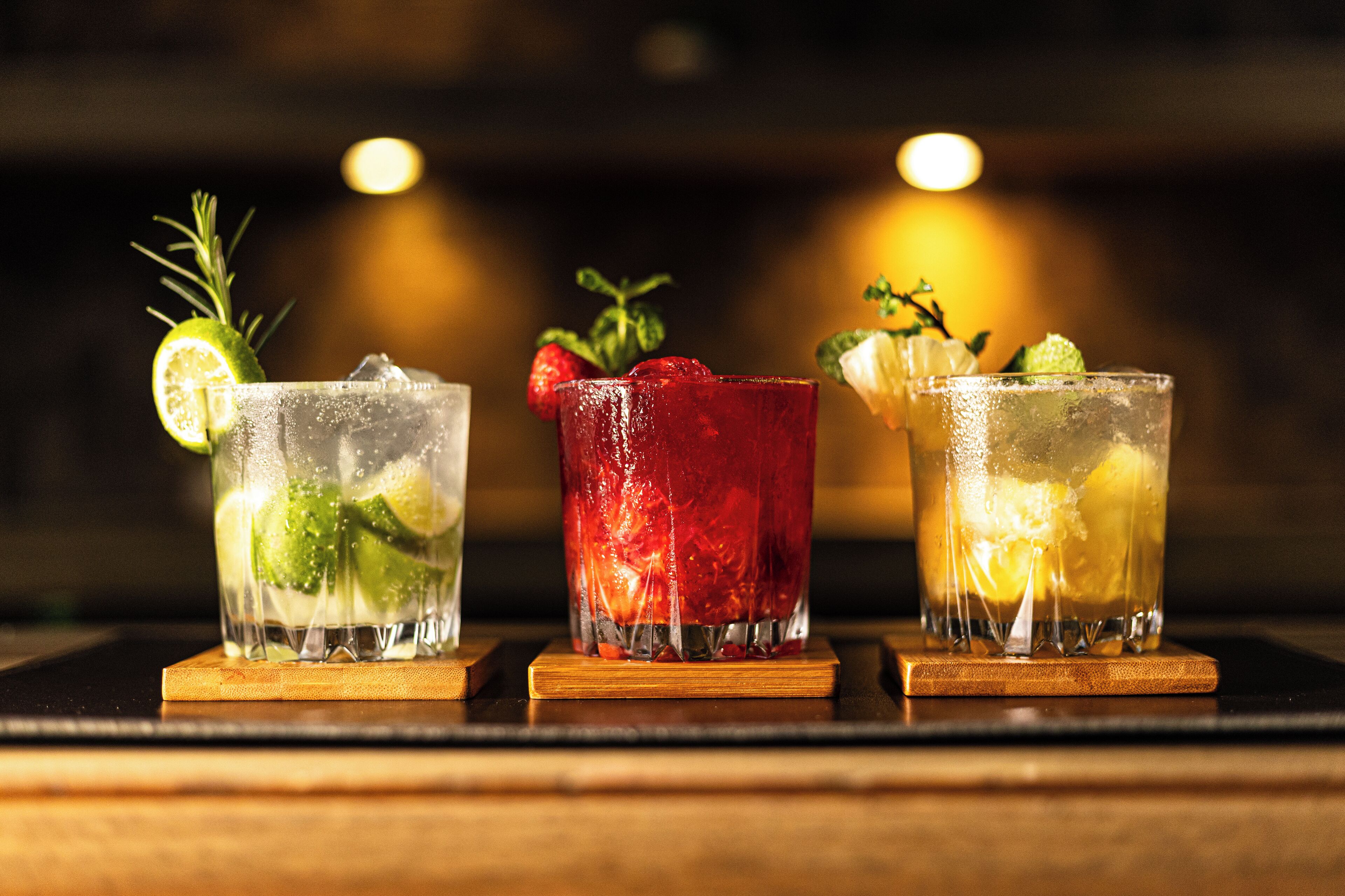 Three glasses of cocktails on a wooden bar counter.