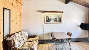 Una habitación con techo de madera, un cuadro en la pared, un sofá, una mesa con sillas y un televisor montado en la pared.
