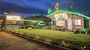 Un motel con un letrero de neón, un coche estacionado adelante y un pequeño edificio con una bandera.