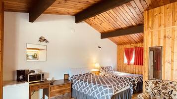 A cozy room with wooden walls and ceiling, a bed with patterned bedding, a desk with a microwave, and a small sofa.